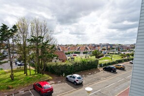 A residential street with parked cars, houses, and a green area with trees and grass. - La Réglisse - À moins d’1 km de la plage (Courseulles-sur-Mer)