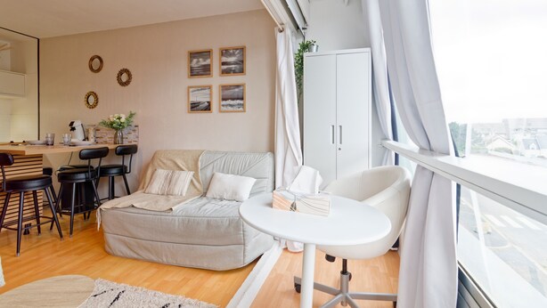 A modern living room with a sofa, a dining area with chairs, a small table, and a view through a large window. - La Réglisse - À moins d’1 km de la plage (Courseulles-sur-Mer)