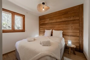 Ein Schlafzimmer mit hölzernem Kopfteil, einem Bett mit weißen Bettwäsche, einer Nachttischlampe und einem Fenster mit Blick auf eine felsige Landschaft.