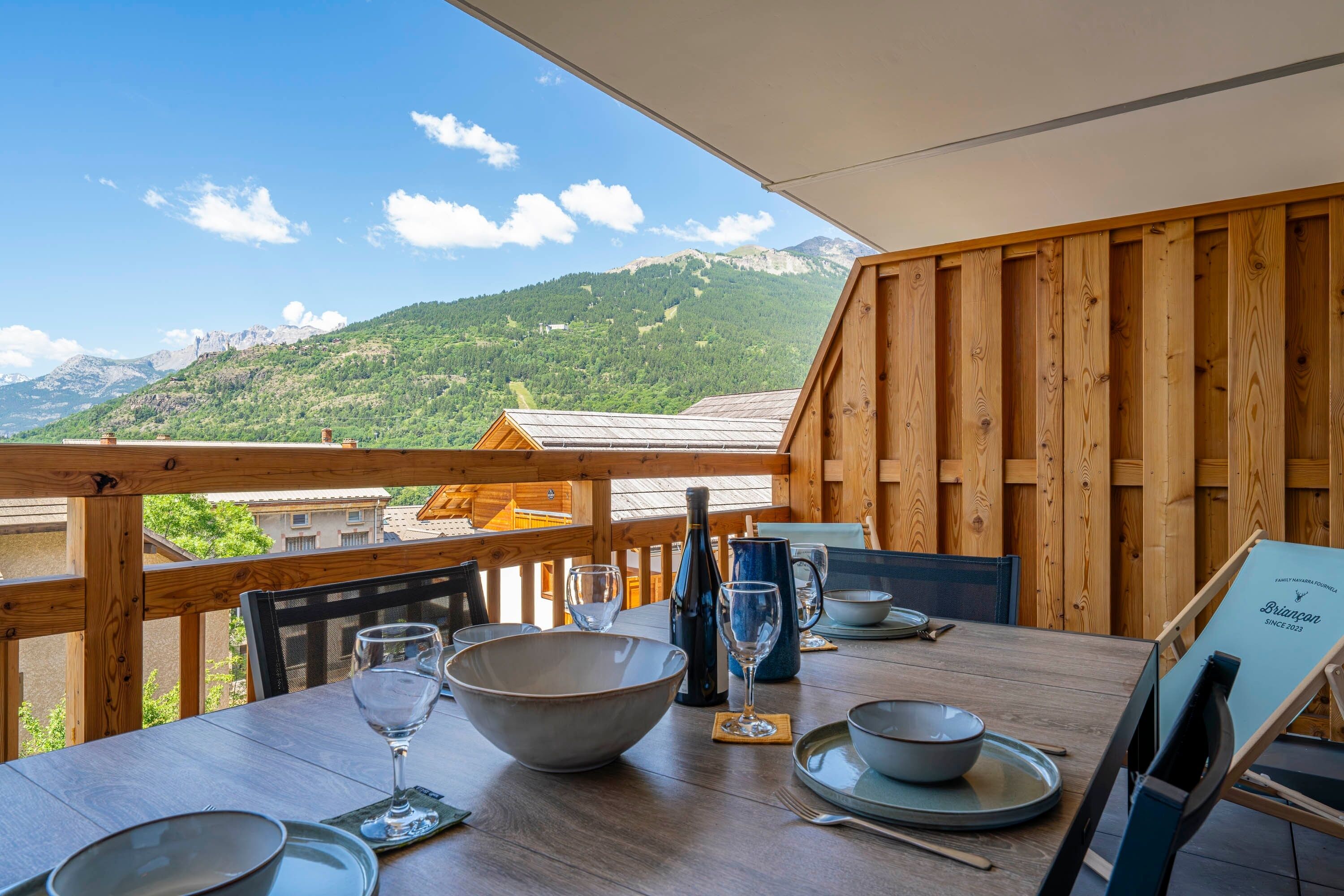 Eine Holzterrasse mit Esstisch, mit Blick auf eine gebirgige Landschaft.