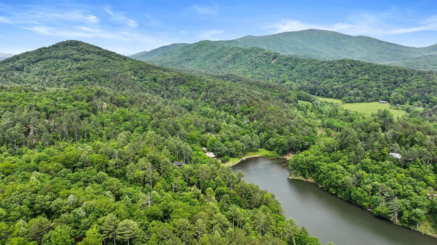 A forested landscape with a river, hills, and a small building.