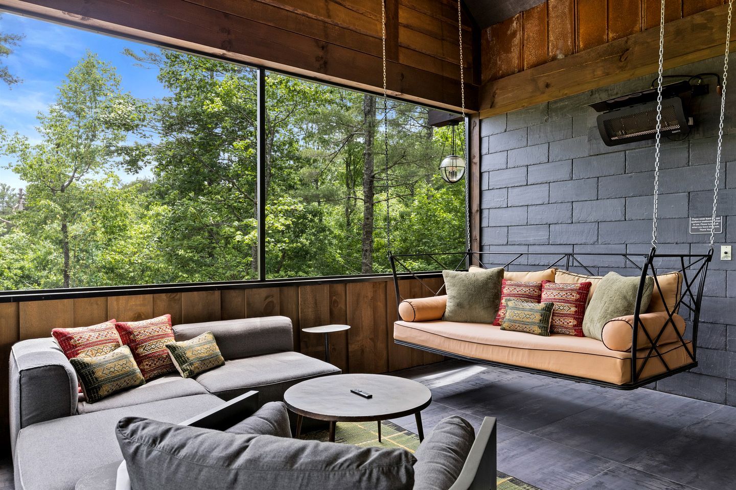 A modern interior with a sofa, a hanging swing, and a view of trees.