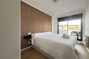 Ein modernes Hotelzimmer mit einem großen Bett, einer Wand aus Holzlatten, einem Fenster mit Balkonblick und einer Deckenleuchte.