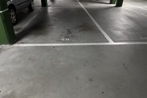 Eine Parkgarage mit Betonböden, markierten Stellplätzen und grünen Säulen.