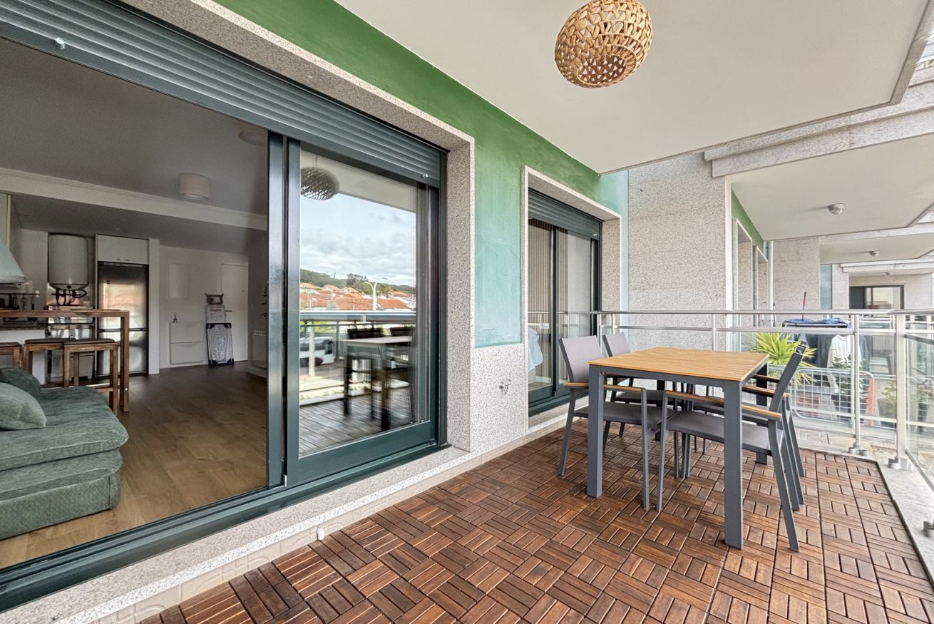 Un appartement moderne doté d’une porte-fenêtre coulissante donnant sur un balcon, d’un coin repas avec une table et des chaises, et d’une cuisine visible à travers la porte.