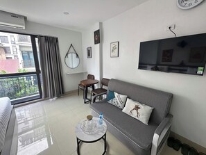 A modern living room with a sofa, a small round table, a TV mounted on the wall, and a balcony with curtains.
