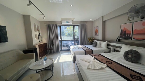 A hotel room with a sofa, two beds, a small table, and a balcony with a view. - Hanoi Homestay Minh Nhat (Hanoi)