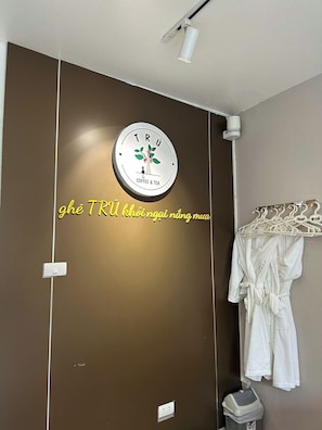 Casa de banho com porta-toalhas, um cesto de lixo e um aviso na parede sobre serviço de café e chá.