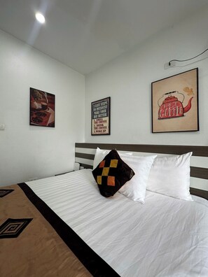A hotel room with a bed, a pillow, a wall-mounted picture, and a wall socket.