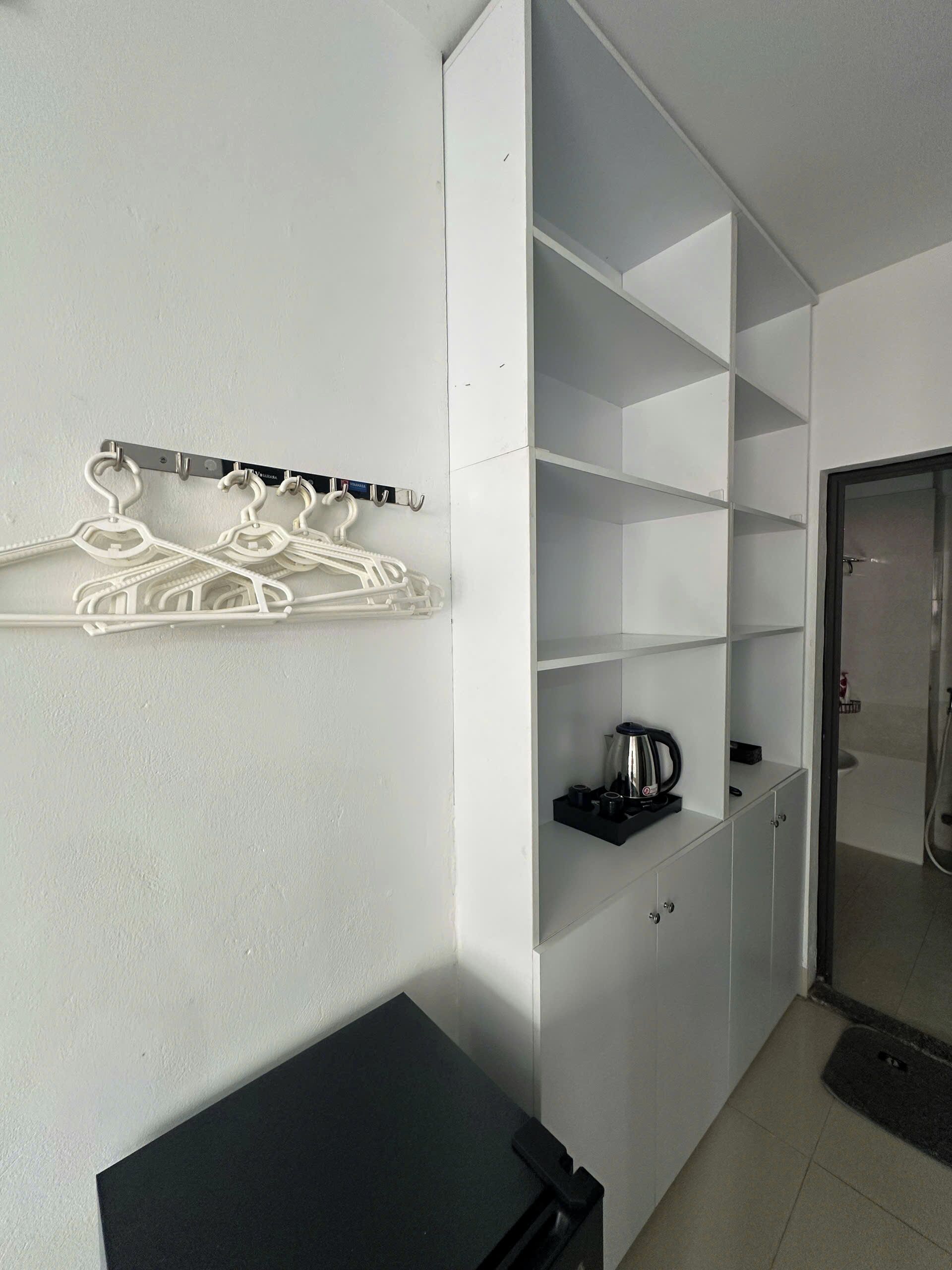 Habitación de hotel con un armario blanco, una mesa negra y un área de ducha.