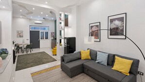 Una sala de estar moderna con un sofá seccional gris, un comedor con mesa y sillas, y una zona de cocina con refrigerador.