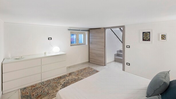 Un dormitorio moderno con cama, mesita de noche y un ventanal pequeño.