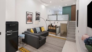 Una sala de estar moderna con un sofá, un refrigerador negro, una escalera y una zona de cocina.