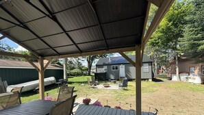 Una terrazza coperta all'aperto con tavolo e sedie, un barbecue e un capanno sullo sfondo.