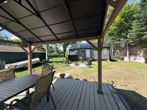 Una terraza techada al aire libre con mesa y sillas, una parrilla y un cobertizo al fondo.