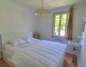 Um quarto com cama, luminária pendente, janela com cortinas, radiador e pia.