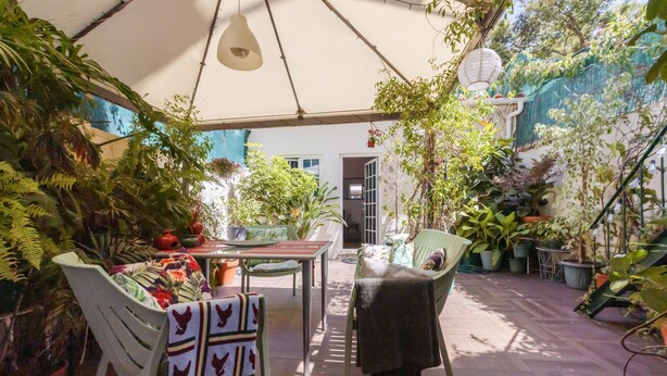 Eine Terrasse im Freien mit Tisch und Stühlen, umgeben von Blumentöpfen und einer hängenden Lampe.