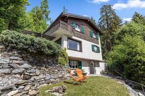 Ein zweistöckiges Haus mit Steinmauer, Balkon und Rasenfläche.