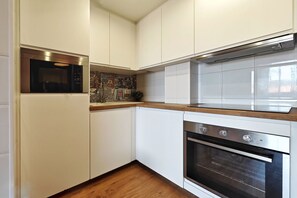 Eine kompakte Küche mit weißen Schränken, einer Mikrowelle, einem Backofen und einer ornamentierten Spritzschutzleiste.