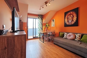 Ein modernes Wohnzimmer mit einer Couch, einem Esstisch mit Stühlen, einem Fernseher auf einem Holzboden und Kunstwerken an den Wänden.