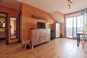 Ein Zimmer mit einem Holzkasten, einem Fernseher, einer Topfpflanze und Meerblick durch ein großes Fenster.
