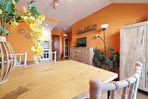 Ein Essbereich mit Holztisch, Stühlen, einer Zimmerpflanze und einem Fernseher auf einer Holzkommode.