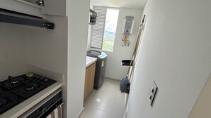 A compact kitchen with a gas stove, a window with blinds, and a mop leaning against the wall. - Premium studio apartment on the Golden Mile (ibague)