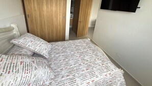 A bedroom with a bed, wooden wardrobe, and a TV mounted on the wall. - Premium studio apartment on the Golden Mile (ibague)