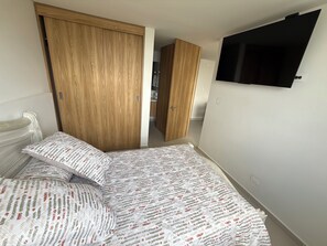 Ein Schlafzimmer mit einem Bett, einem Holzschrank und einem an der Wand befestigten Fernseher.