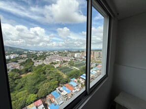 Blick aus dem Fenster auf eine Stadtlandschaft mit Gebäuden, Grünflächen und blauem Himmel.