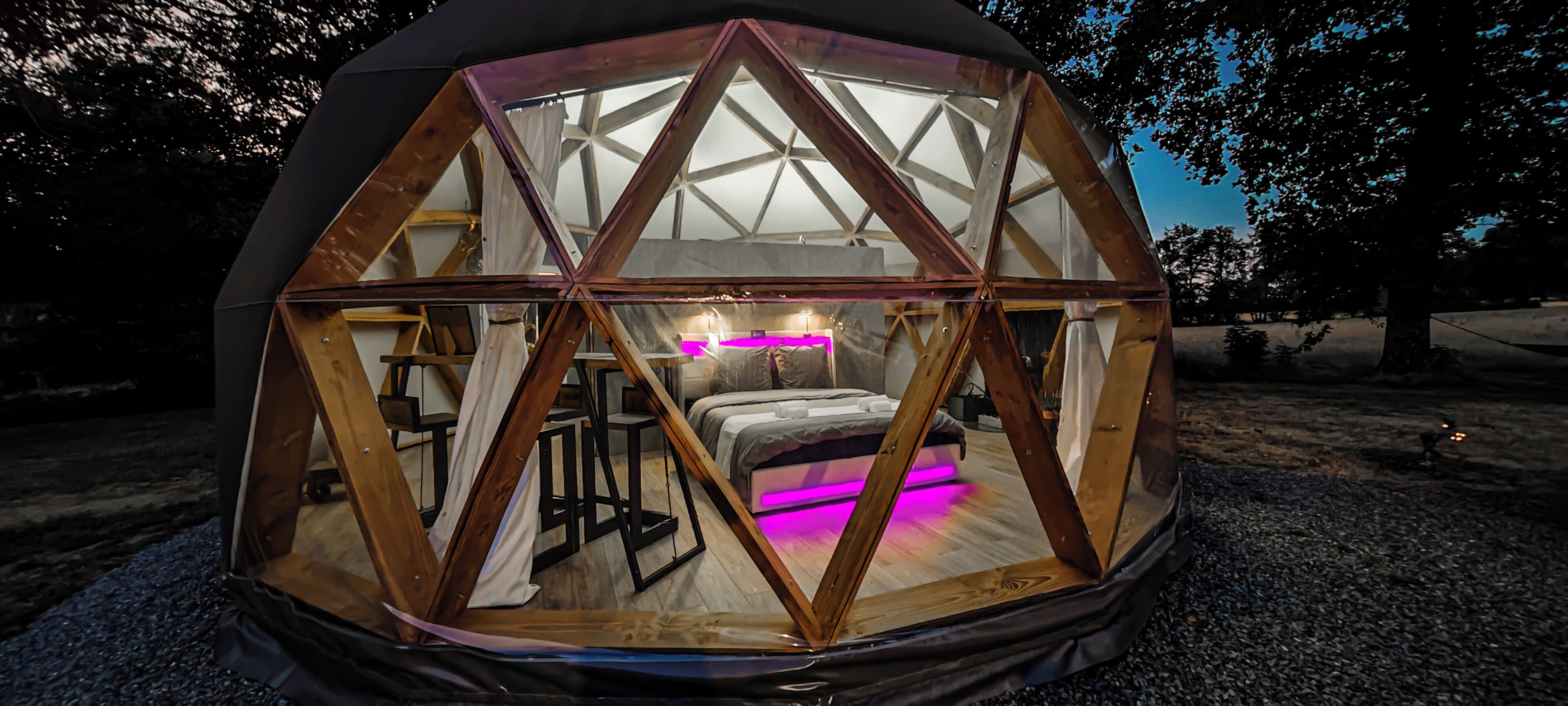 Una struttura a cupola geodetica con un letto, un tavolo e una sedia all'interno.