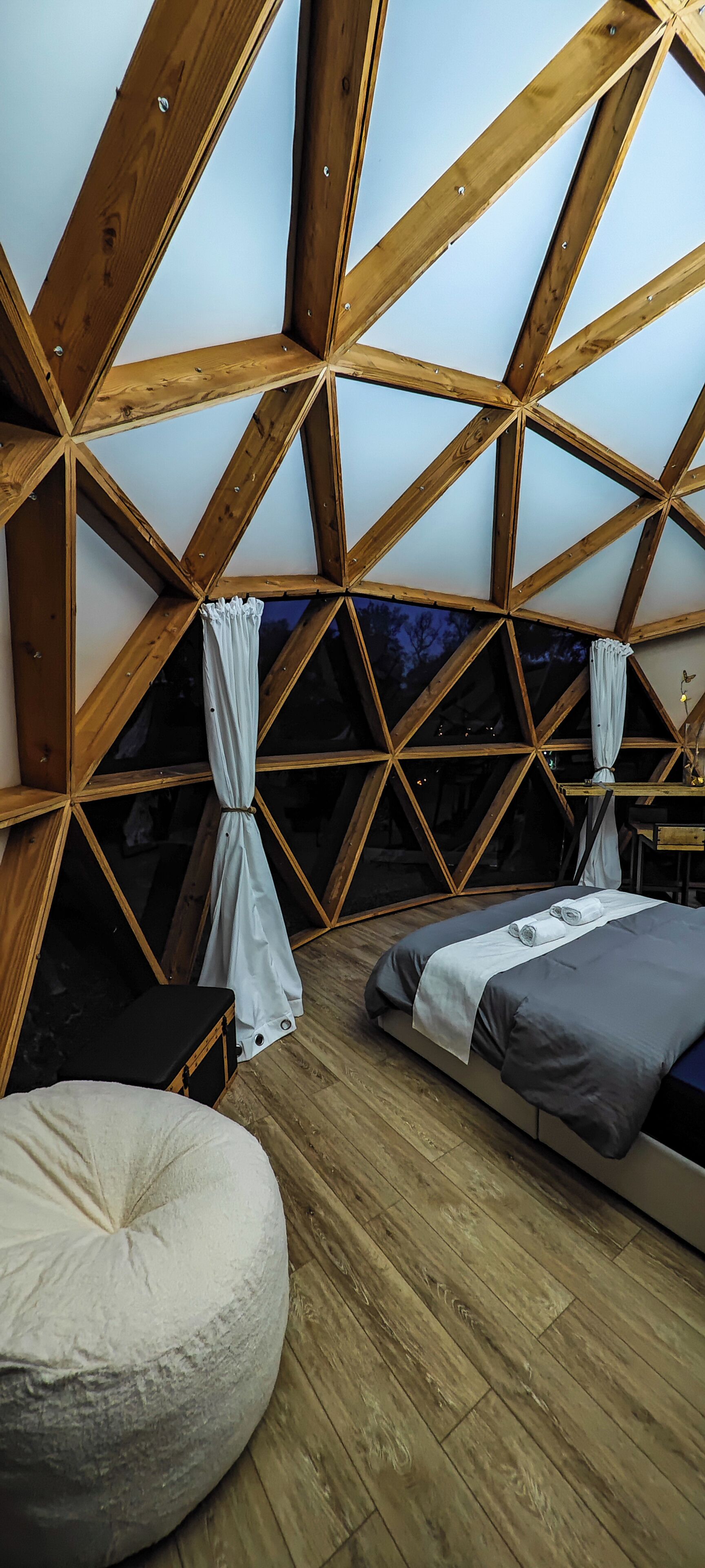 A triangular room with wooden beams, two beds, a round seating area, and a view of the night sky.