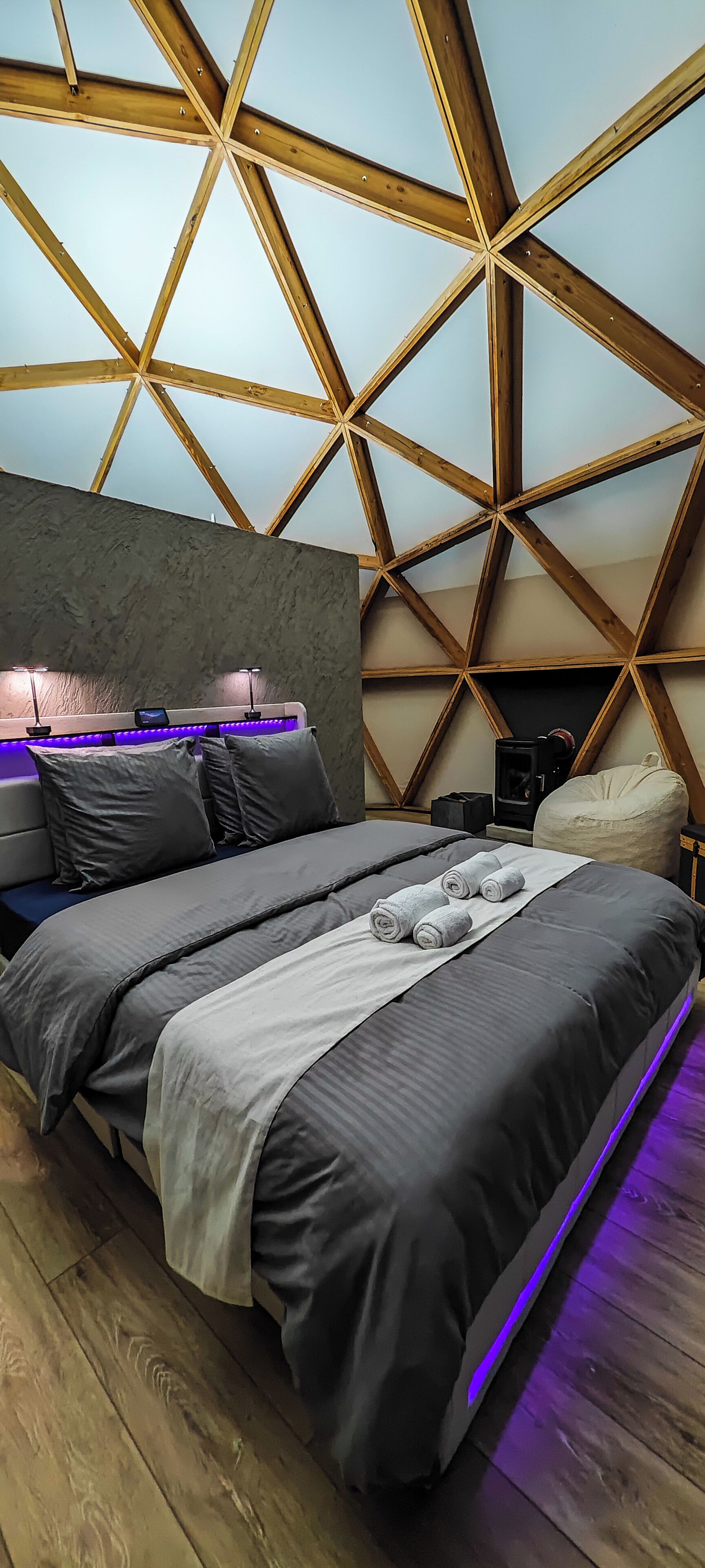 Un dormitorio moderno con un diseño geométrico en el techo, una cama con ropa de cama gris y un pequeño calentador.