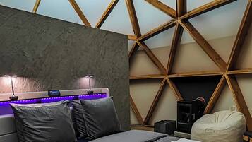 Un dormitorio moderno con un diseño geométrico en el techo, una cama con ropa de cama gris y un pequeño calentador.