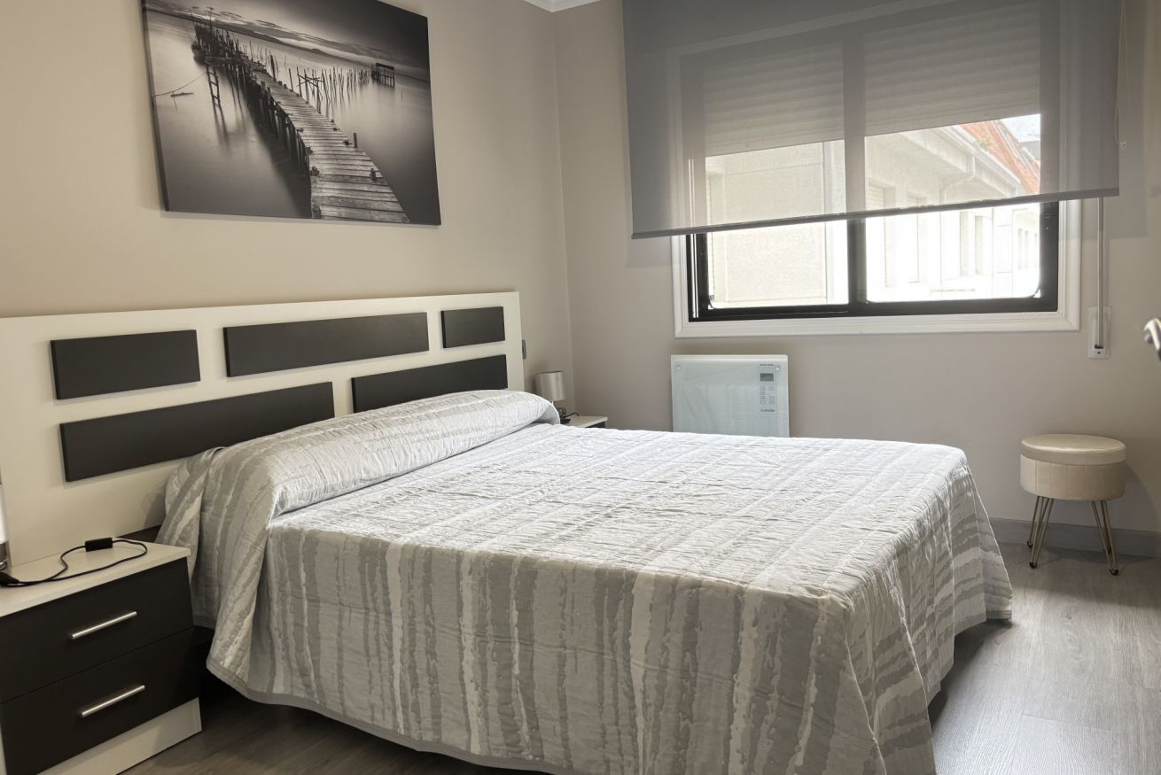 A bedroom with a bed, a nightstand, a wall-mounted picture, a window with blinds, and a radiator.