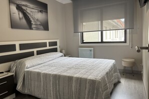Une chambre à coucher comprenant un lit, une table de chevet, une commode, une fenêtre avec des stores et une œuvre d’art accrochée au mur.