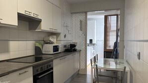 Cozinha moderna com armários brancos, mesa de jantar de vidro e vista para a área de serviço.