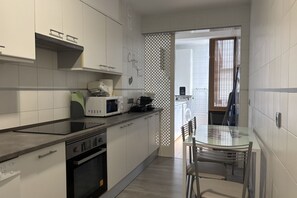 A modern kitchen with white cabinets, a glass dining table, and a view into the laundry area. - Desconectaengalicia Gaviota, 50 meters from Silgar Beach (Pontevedra)