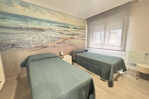 A room with two beds, a beach mural, a window with blinds, and a small bedside table with a lamp. - Desconectaengalicia Gaviota, 50 meters from Silgar Beach (Pontevedra)