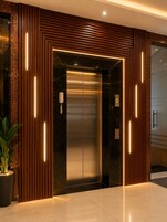 Un ascensor moderno con detalles metálicos, flanqueado por paneles de madera e iluminado por tiras de luz verticales.