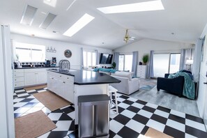 A spacious living area with a kitchen, a sofa, and a television. - Welcome to The Coastal Crown, your ultimate luxury beach getaway! 👑<br>✨ Top-Floor Penthouse<br>🏖️ Steps to the Beach<br>🌊 Balcony Ocean Views<br>🛁 Master Suite Jacuzzi<br>📺 85" TV & Skylights (North Myrtle Beach)