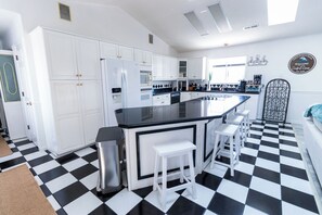 A kitchen with white cabinets, a black countertop, and a checkered floor. - Welcome to The Coastal Crown, your ultimate luxury beach getaway! 👑<br>✨ Top-Floor Penthouse<br>🏖️ Steps to the Beach<br>🌊 Balcony Ocean Views<br>🛁 Master Suite Jacuzzi<br>📺 85" TV & Skylights (North Myrtle Beach)