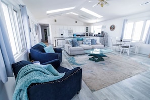 A modern living room with a sofa, armchairs, a coffee table, and a kitchen in the background. - Welcome to The Coastal Crown, your ultimate luxury beach getaway! 👑<br>✨ Top-Floor Penthouse<br>🏖️ Steps to the Beach<br>🌊 Balcony Ocean Views<br>🛁 Master Suite Jacuzzi<br>📺 85" TV & Skylights (North Myrtle Beach)