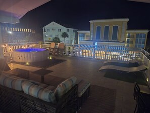 En takterrass med ett bubbelbad, en sittgrupp och utsikt över en byggnad med stora fönster.