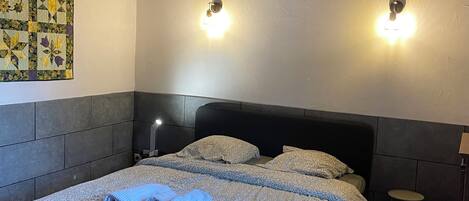 Un dormitorio con techo de madera, una cama acolchada, dos lámparas fijadas a la pared y un tapiz acolchado en la pared.