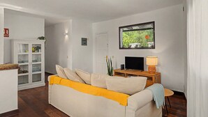Ein Wohnzimmer mit einer Couch, einem an der Wand montierten Fernseher, einer Vitrine und einer Lampe auf einem Holztisch.
