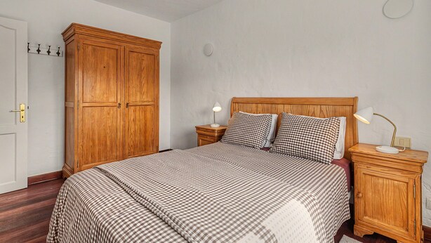 Ein Schlafzimmer mit großem Holzschrank, einem Bett mit karierter Bettwäsche, Nachttischlampen und einem Nachttisch.