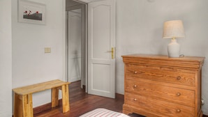 Ein Zimmer mit einem hölzernen Schminktisch, einem Nachttisch, einer Lampe und einer Tür zu einem anderen Raum.