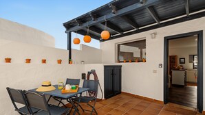 Eine Terrasse im Freien mit Tisch und Stühlen, einer Tür und einem Fenster mit Jalousien.