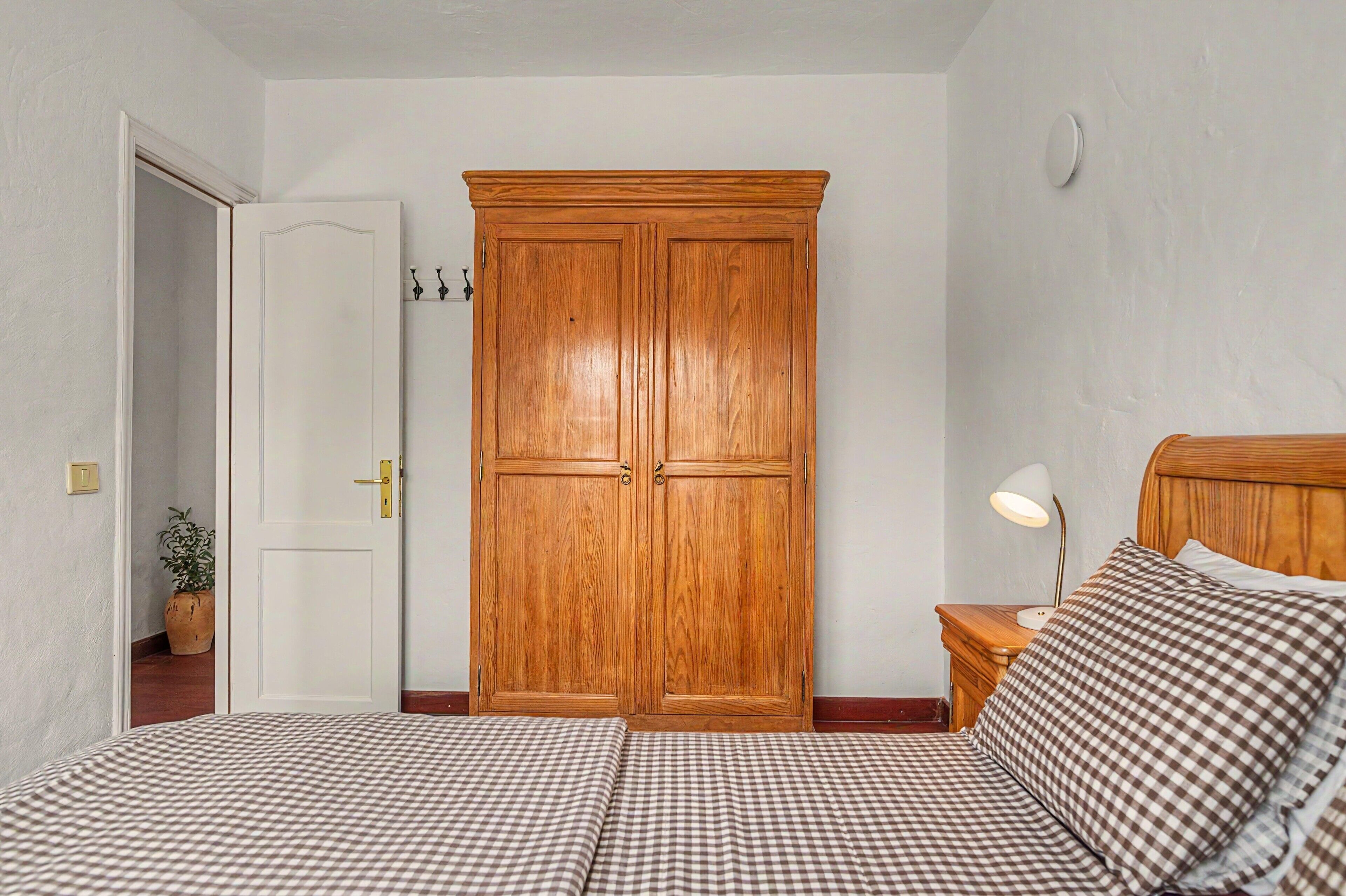 Una camera da letto con un letto matrimoniale, un'armadietto in legno, un comodino con una lampada e una pianta in vaso.